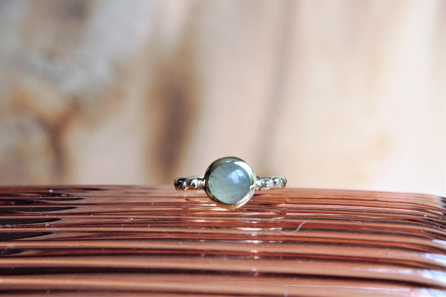 Gouden ring met kleine blauwe steen op koperoranje lint