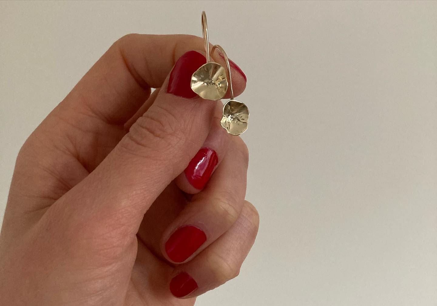 Hand met rode nagels houdt gouden hartvormige oorbel