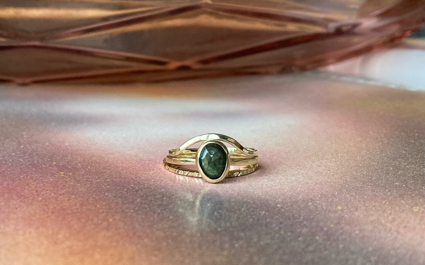 Gouden ring met kleine groene steen op perzikkleurige ondergrond