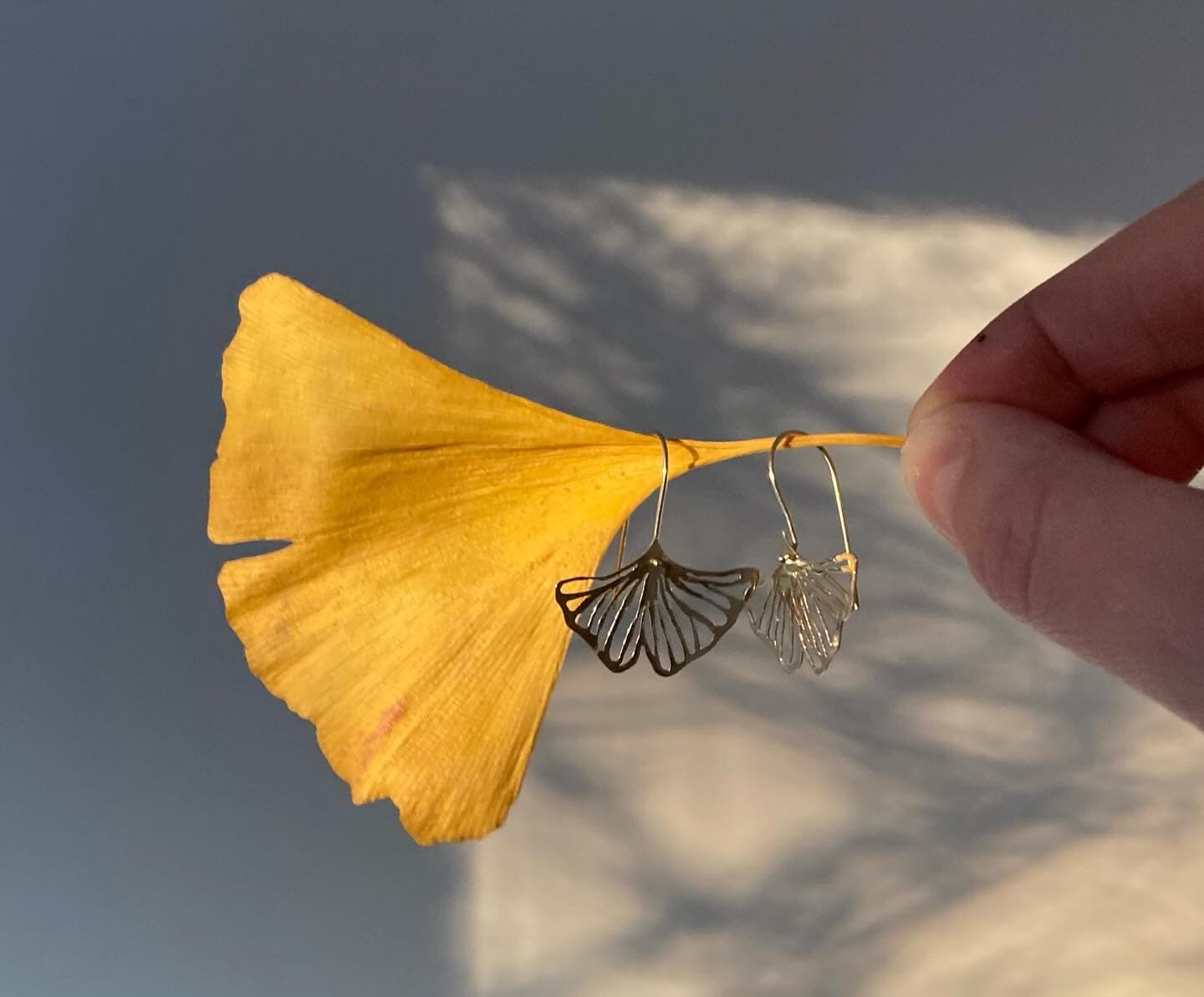 Hand houdt gouden oorbel vast bij ginkgoblad