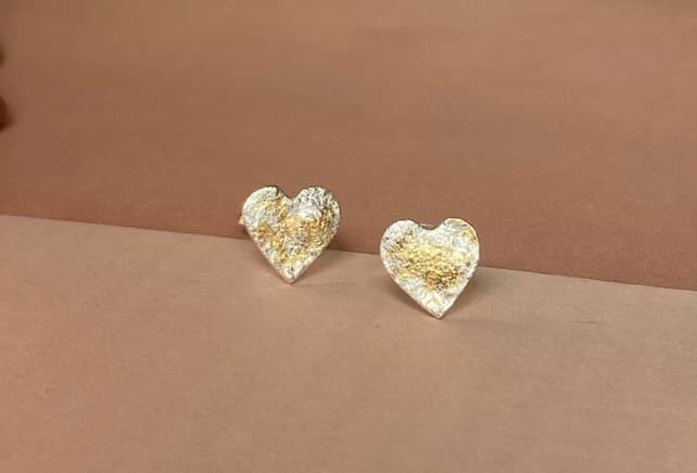 Paar hartvormige gouden oorbellen op perzikkleurige ondergrond