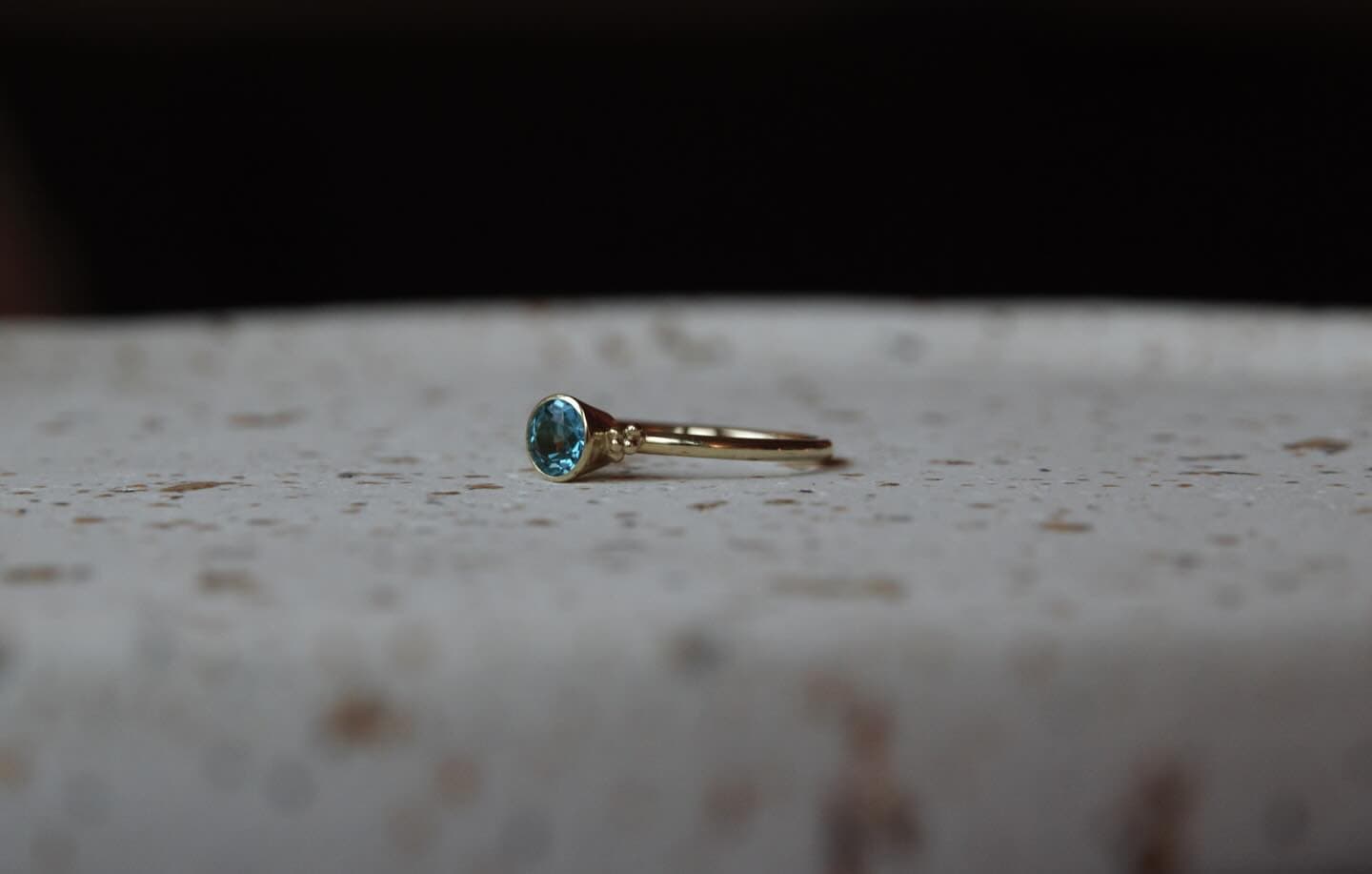 Gouden ring met klein helder steentje op zand-beige ondergrond