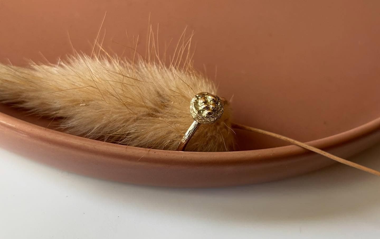 Gouden ring tussen droogbloemen op perzikkleurige ondergrond