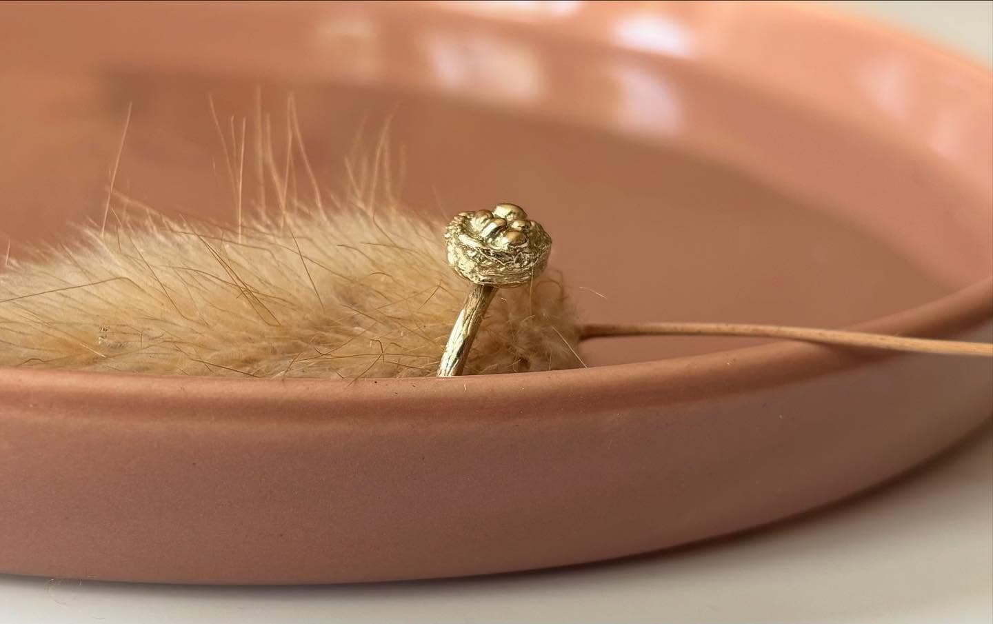 Gouden ring met klein steentje op perzik vlak met droogbloem