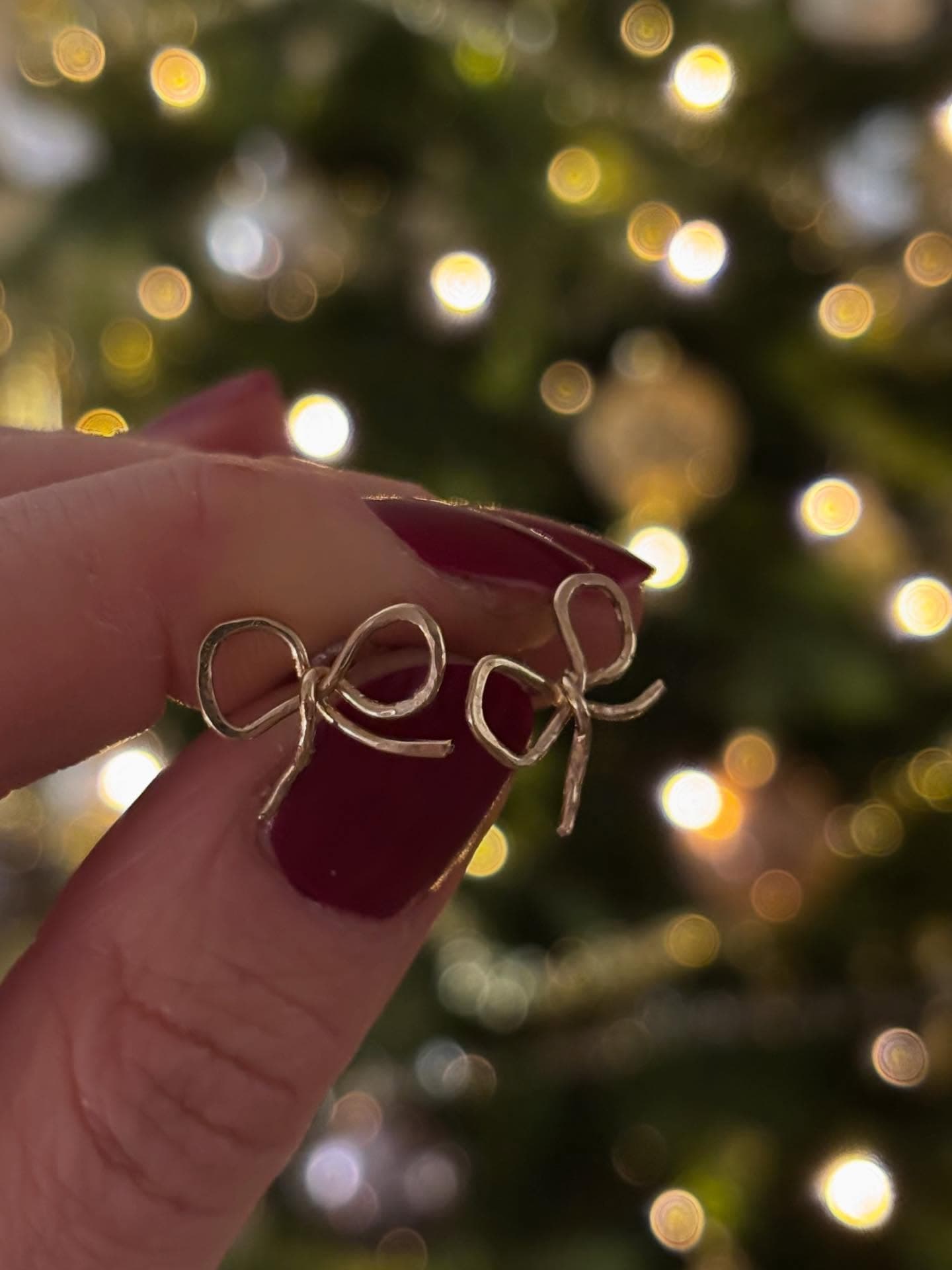 Hand met rode nagels houdt gouden oorbel bij kerstboom