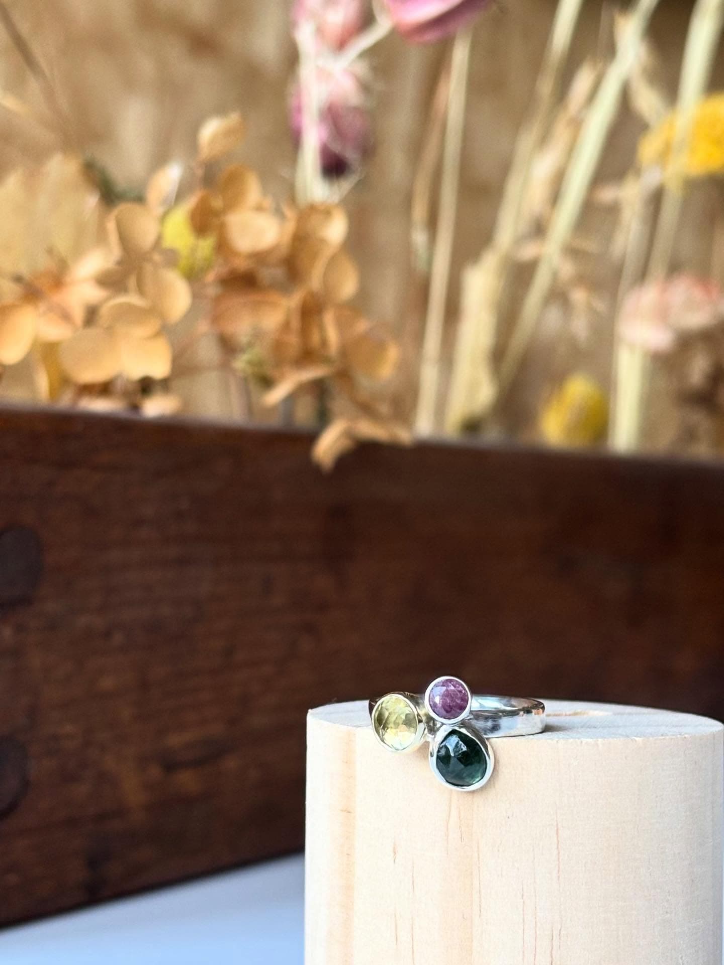 Gouden ring met klein steentje op houten blok bij droogbloemen
