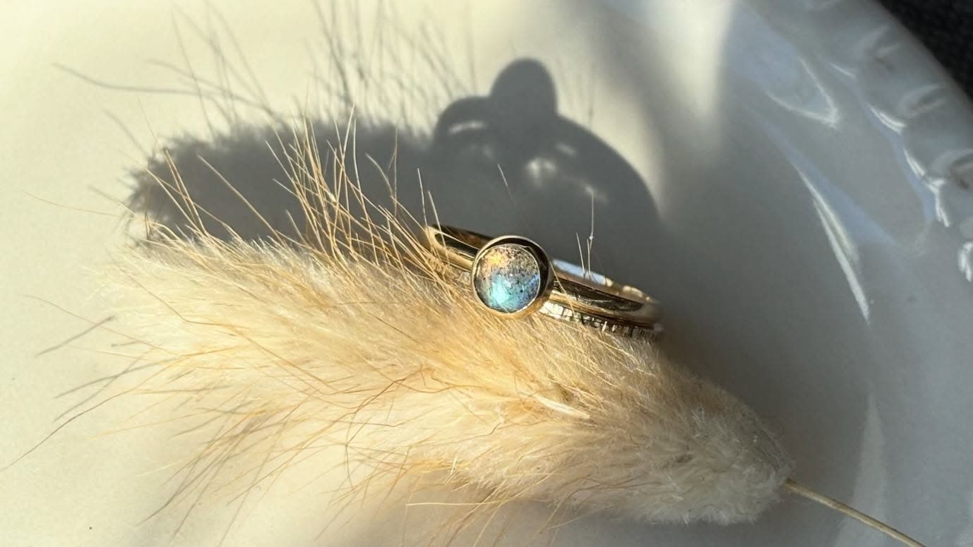 Gouden ring met kleine blauwe facetsteen op beige veren